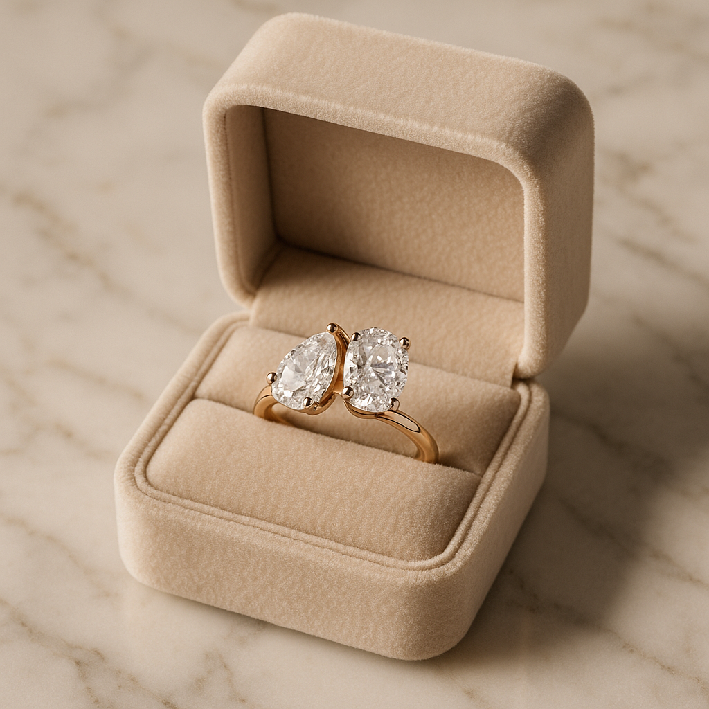 Toi et Moi engagement ring with pear and oval-cut natural diamonds set in rose gold, displayed in a beige velvet box on a marble surface.