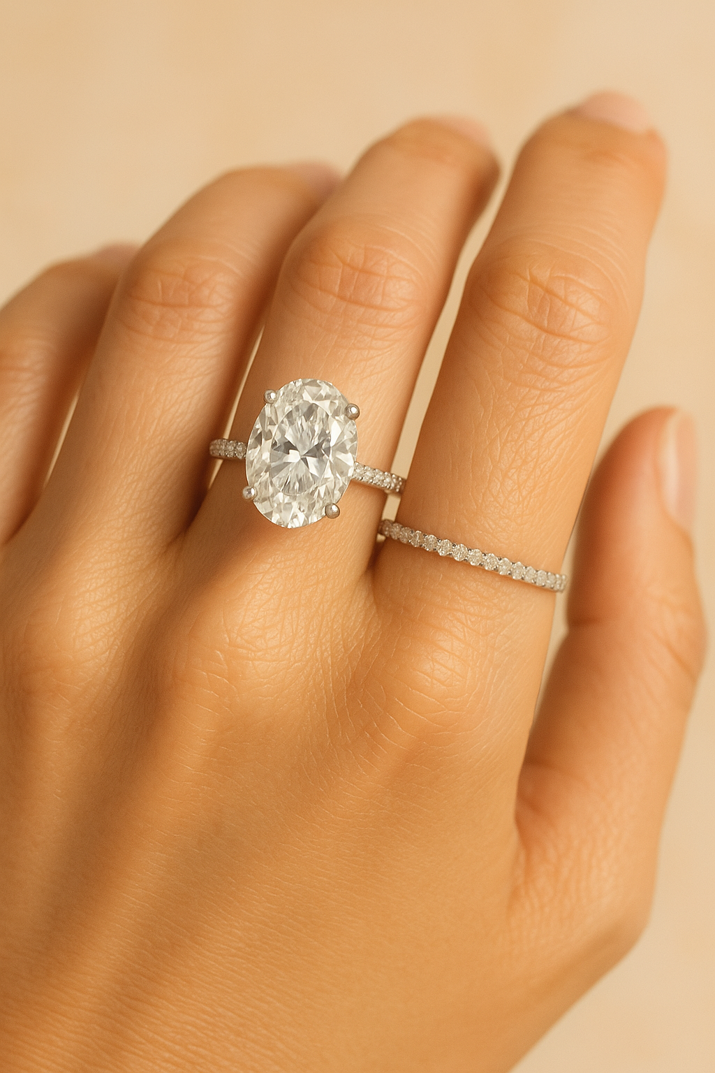 Close-up of hand wearing 5-carat oval diamond engagement ring with pavé band and eternity ring, luxury editorial look.